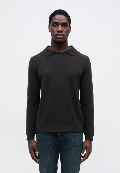 Ciemnoszary wełniany sweter z prążkowanym dołem i kołnierzem, z długimi rękawami i klasycznym krojem, noszony z niebieskimi dżinsami.