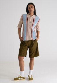 Collared, short-sleeve knitted polo in peach and blue, featuring vertical red stripes; paired with olive green shorts and sneakers.