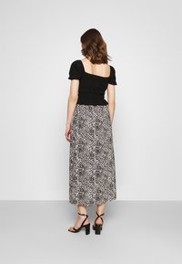 Top nero smock con maniche a palloncino corte abbinato a una lunga gonna maculata. Modella che indossa sandali neri con tacco.