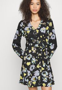Vestido envolvente preto com flores, apresentando mangas compridas, decote em V e cintura com laço, adornado com flores multicoloridas em roxo e amarelo sobre um fundo escuro.