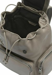 Sac à dos en cuir gris clair avec un dessus cintré, doté d'une poche zippée et d'accents en métal, texture lisse et doublure en tissu foncé.
