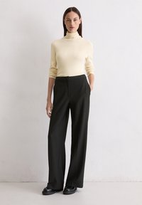 Pull en grosse maille crème à col roulé avec des manches longues, associé à un pantalon large noir taille haute et des chaussures à plateforme noires.