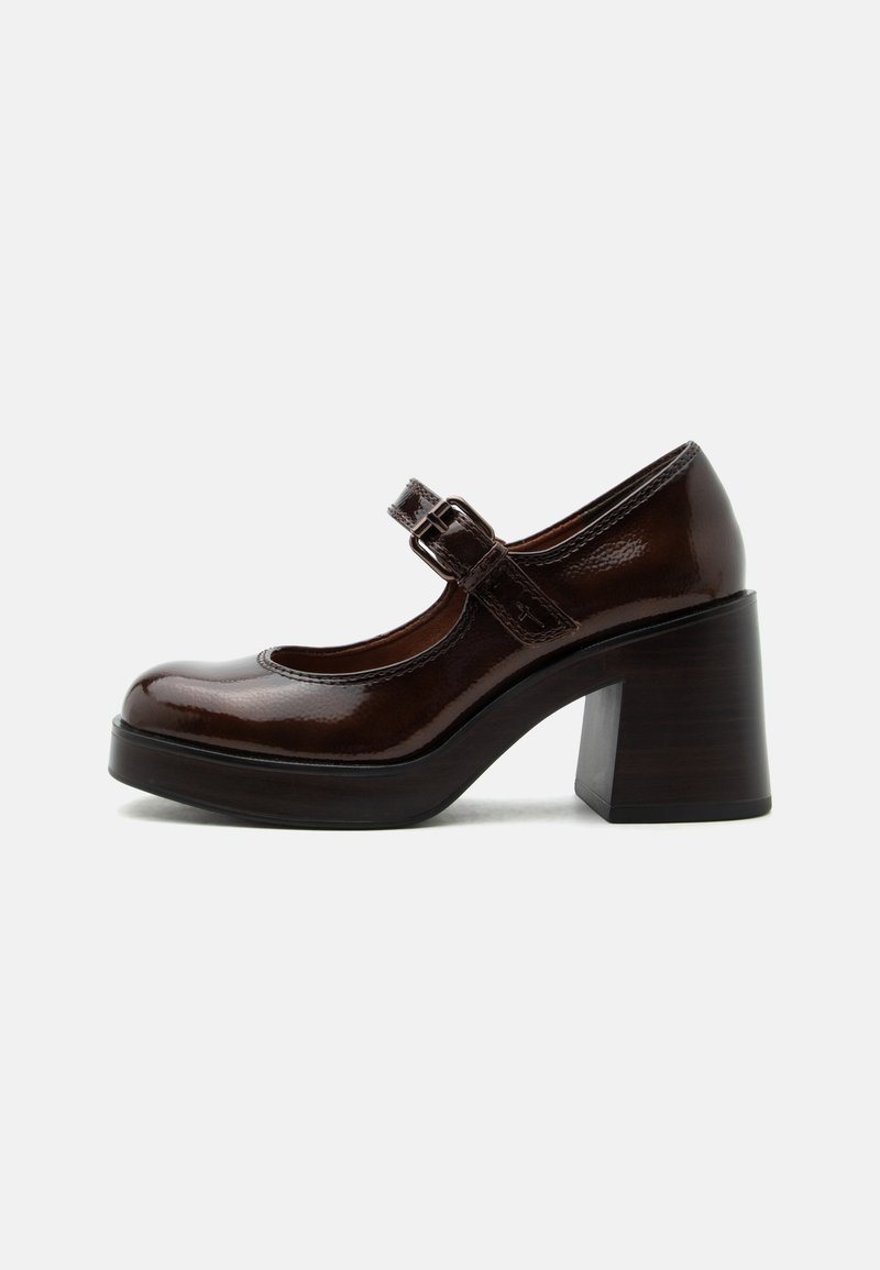 Chaussure Mary Jane en cuir verni marron foncé avec un talon haut épais et une bride ajustable à boucle sur fond gris clair.