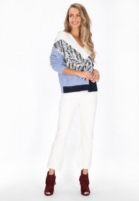 Sweter dzianinowy w jasnym niebieskim kolorze z cekinowym trójkątnym wzorem w srebrnym i ciemnoniebieskim kolorze. Połączony z białymi dzwonami i bordowymi botkami z frędzlami.