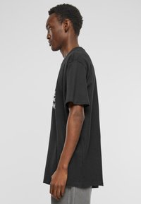 T-shirt en coton noir à manches courtes, coupe décontractée et détail sur les coutures latérales. Présente un design graphique sur la poitrine dans une couleur contrastante.