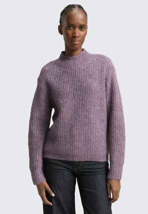 Pull en tricot violet avec une texture côtelée, col montant et manches larges, associé à un jean en denim noir. Matière douce et coupe décontractée.