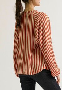 Rood en crème gestreepte blouse met een losse pasvorm, lange mouwen en een ronde halslijn. De stof lijkt soepel en lichtgewicht.