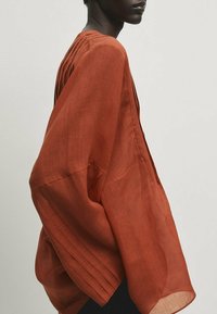 Rostrød, løst siddende bluse med plisserede detaljer og brede ærmer, fremstillet af letvægts, tekstureret stof.