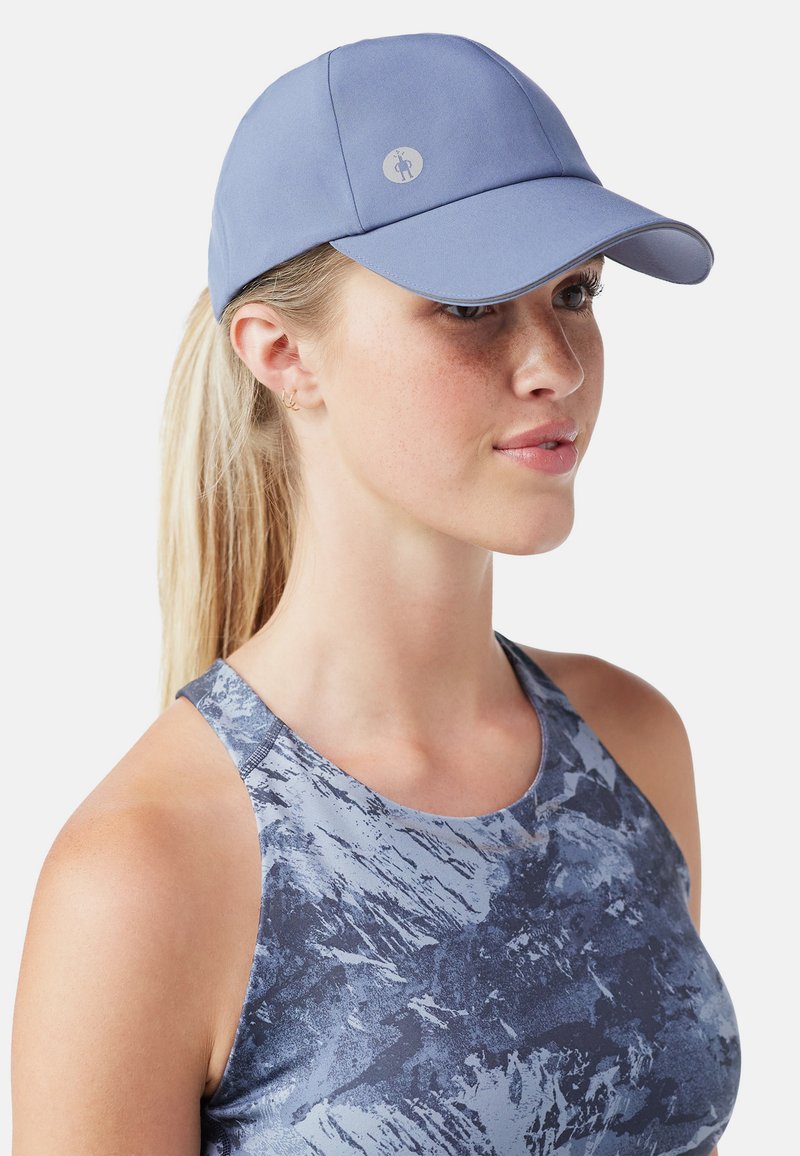 Ljusblå keps med en böjd skärm och liten logotyp. Slät tygtextur, justerbar rem bak, kombinerad med en mönstrad sporttopp.