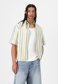 Camicia a maniche corte con bottoni, a righe gialle e grigie. Tessuto leggero con un taglio rilassato, abbinata a una canotta bianca e jeans blu.