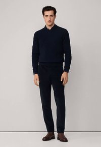 Marineblauer strukturierter Pullover mit rundem Ausschnitt, kombiniert mit passenden, schmal geschnittenen Hosen und braunen Lederschuhen. Einfaches, modernes Design.