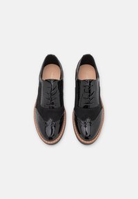 Scarpe oxford in pelle verniciata nera con upper in suede, punta arrotondata e perforazioni decorative. Sole cucito color beige per un contrasto.