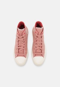 High-top sneakers in soft pink fabric, featuring white rubber toe cap, contrasting laces, and logo accents on the sides and tongue.