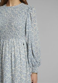 Niebieska i biała sukienka w kwiatowy print z marszczonym bodicem i bufiaste rękawy. Miękka tkanina z lekko opadającą spódnicą i marszczonymi mankietami.