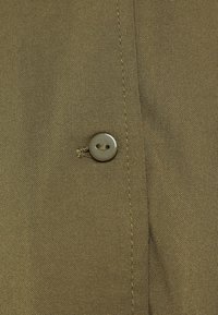 Tessuto verde oliva con un singolo bottone rotondo grigio-verde cucito vicino a una cucitura verticale.