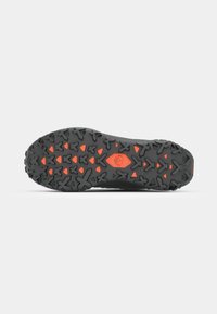 Semelle de chaussure robuste noire et orange avec des crampons triangulaires et en forme de croix conçus pour l’adhérence et l’usage en extérieur.