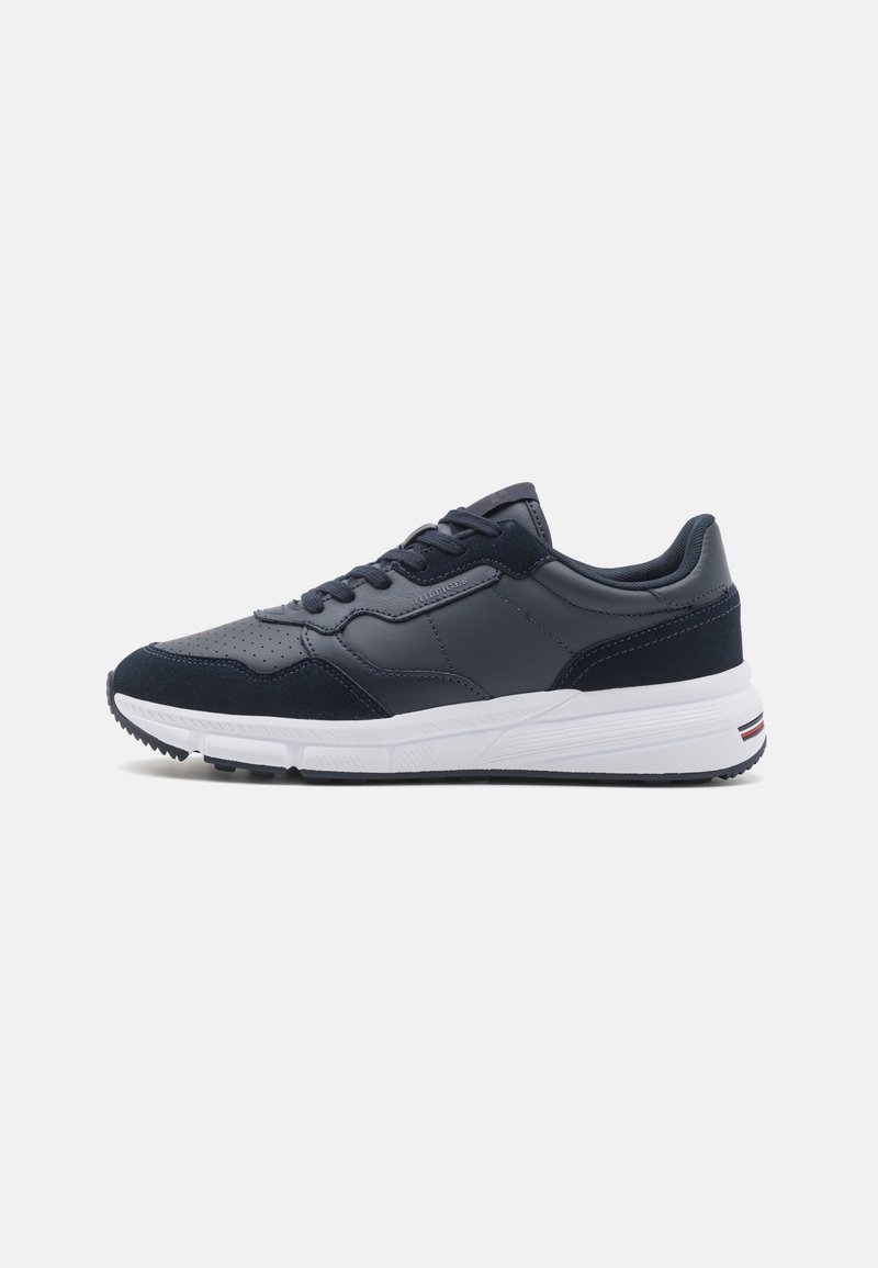 Baskets noires et gris foncé avec embout perforé, design à lacets, semelle blanche rembourrée et détail subtil du logo sur le côté et le talon.