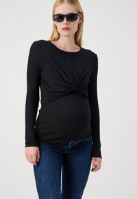 Top negro de manga larga con ribetes y diseño frontal retorcido, combinado con jeans azul oscuro. La tela parece suave y elástica.