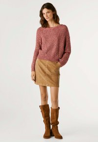 Χοντρή, ροδόχροση πλεχτή ζακέτα με μακριά μανίκια, συνδυασμένη με καφέ κοτλέ μίνι φούστα και καφέ σουέτ μπότες μέχρι το γόνατο.