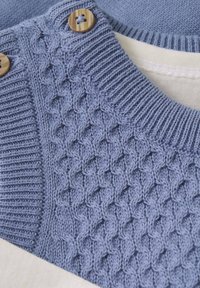 Strikket sweater i lys blå farve, med tekstureret mønster på den ene side, kontrasterende ribstrikket halsudskæring og træknapper til lukning.