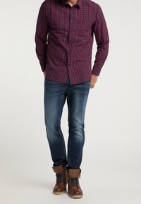 Koszula w kratę w kolorze bordowym i granatowym z długim rękawem oraz kieszonką na piersi, zestawiona z ciemnymi, dopasowanymi dżinsami i brązowymi butami na sznurówki.