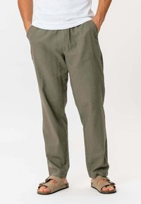 Lette, olivengrønne linnedbukser med lige snit, sidelommer og løst fit. Sammen med brune sandaler med sløjfeaccent.