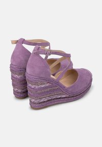 Scarpe con zeppa in suede viola, con cinturini incrociati, caratterizzate da una texture intrecciata e dettagli metallici sulla piattaforma a strati.