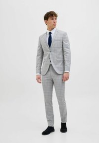 Lys grå jakkesæt med et ternet mønster, der har en enkeltbrystet jakke, slim-fit bukser og et marineblåt slips. Sorte sko fuldender looket.