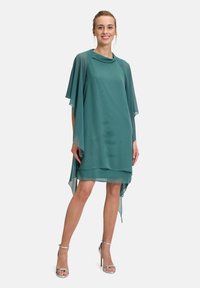 Abito in chiffon turchese con un design a strati leggero. Presenta maniche corte e una silhouette fluida, completato da sandali con tacco alto argentati.