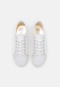 Valkoiset tennarit, jotka on valmistettu sileästä nahasta, joissa on pyöreä kärki, litteät nauhat ja huomaamaton logo sisäpohjassa. Minimalistinen muotoilu, ei näkyviä kuvioita.