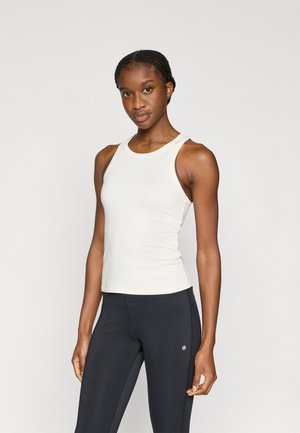 Hellbeiges Tanktop mit rundem Ausschnitt und ärmellosem Design aus glattem Stoff. Kombiniert mit schwarzen, eng anliegenden Leggings.