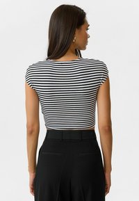Zwart-wit gestreepte crop top met kapmouwen, voorzien van een ronde halslijn en een gladde textuur, gecombineerd met op maat gemaakte zwarte broeken.