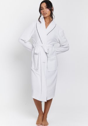 Robe blanche en tissu pelucheux, avec un col châle, des garnitures noires, une ceinture à la taille et deux poches à l'avant, au design mi-long.