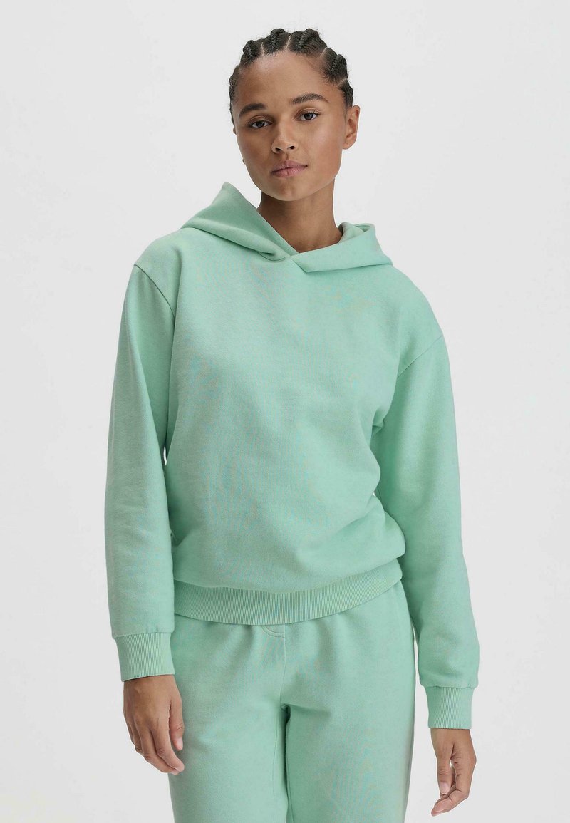 Mintgrüner Kapuzenpullover mit Rippbündchen und Saum. Weicher Textil; getragen mit passenden Hosen. Minimalistisches Design, keine sichtbaren Muster.