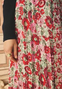 Robe florale présentant un motif rose et vert avec des fleurs rouges et roses ; texture lisse ; associée à une manche côtelée noire et une bague en or.