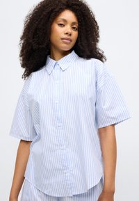 Ανοιχτό μπλε και λευκό ριγέ πουκάμισο με κουμπιά, κοντά μανίκια, γ ιακά, κατασκευασμένο από λείο ύφασμα, διαθέτει στρογγυλεμένο τελείωμα και κουμπιά μπροστά.