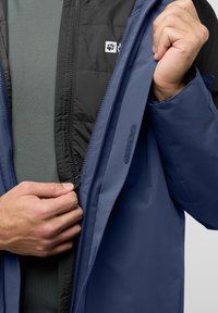 Veste bleue avec une doublure isolante noire, dotée d'une fermeture éclair à l'avant et d'une poche. Texture lisse avec une finition mate et des couches contrastantes.
