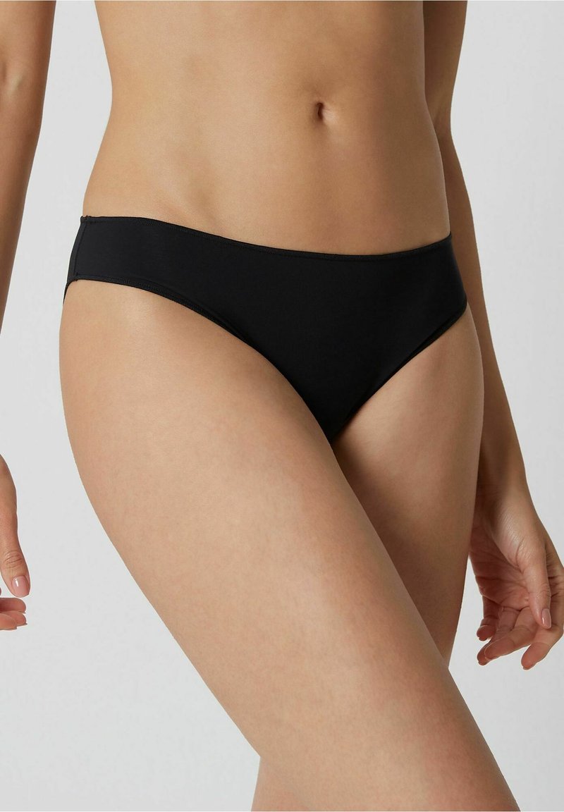 Svart bikiniunderdel med låg midja, slät yta och minimal täckning. Tyget verkar vara elastiskt och figurnära.