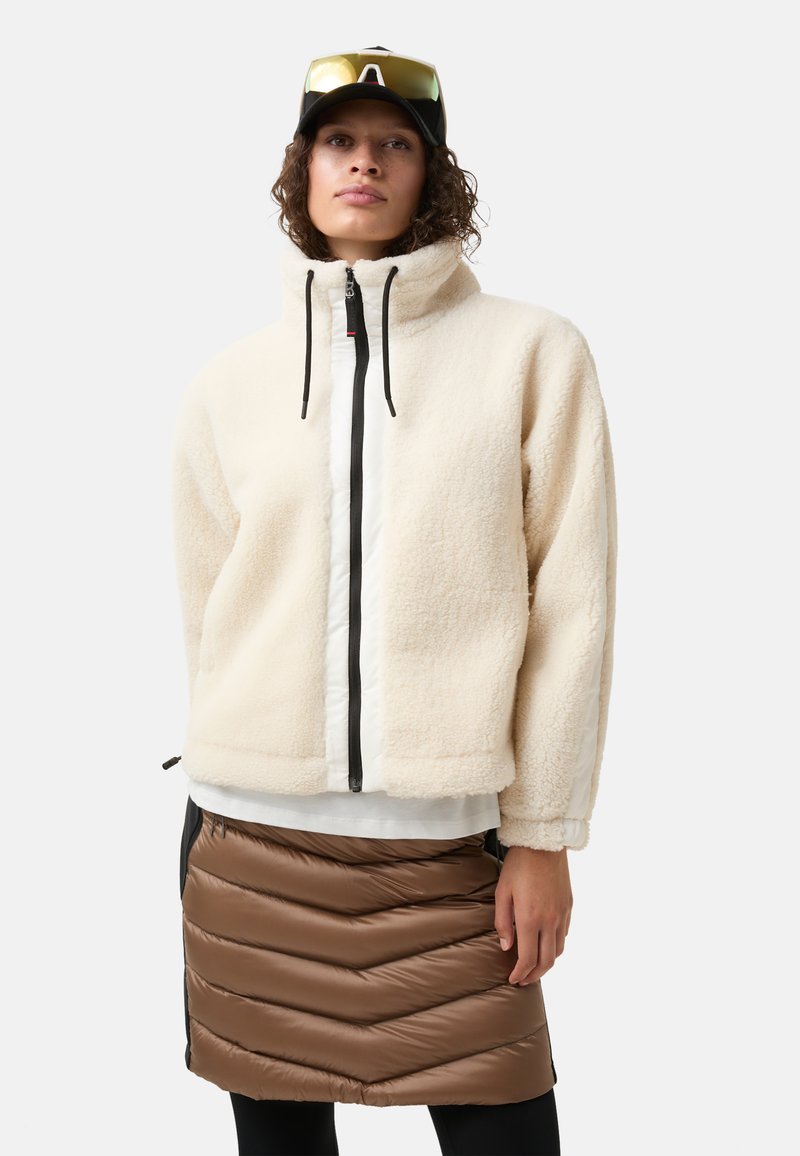 Fleecejakke i off-white med høj krave og sort lynlås, kombineret med en brun quiltet polstret nederdel med chevron-mønster.