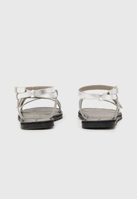 Zilveren lederen sandalen met platte zwarte rubberen zolen, voorzien van kruislings banden en een verstelbare enkelband. Getextureerde voetbed.