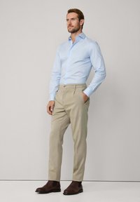 Light blue button-up shirt with long sleeves, paired with beige pleated trousers and brown leather ankle boots. Simple and tailored design.