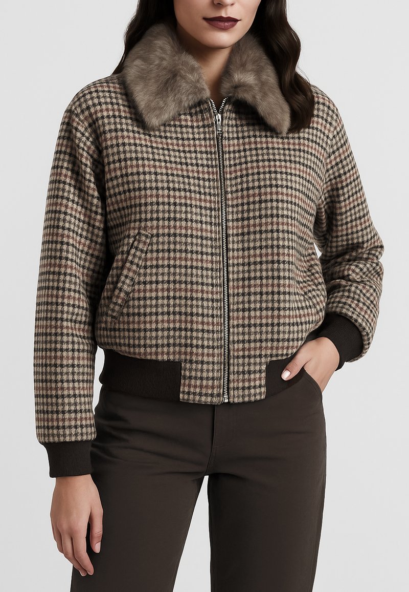 Donna che indossa una giacca a quadri con zip e colletto di pelliccia, con polsini e fascia in vita a coste di colore marrone scuro, abbinata a pantaloni scuri.