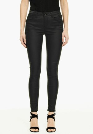 Pantalon skinny en simili cuir noir avec poches avant, fermeture à bouton et à fermeture éclair. Texture lisse et design moulant, associé à des sandales à talons aiguilles noires.