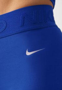 Gros plan sur la ceinture d'un legging de sport bleu avec un logo Nike en relief et un swoosh blanc Nike sur le tissu en dessous.