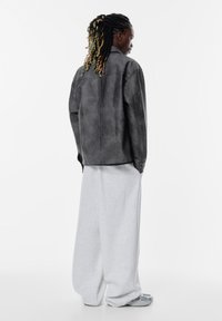 Grå læderjakke med en afslappet pasform, enkelt frontknap og syningsdetaljer, parret med løse grå sweats og grå sneakers.