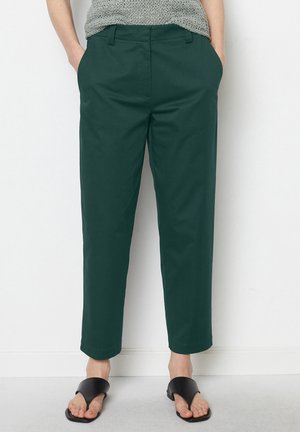 Dunkelgrüne, cropped Chinos mit Seitentaschen, glattem Stoff und geradem Bein-Design, kombiniert mit schwarzen Slide-Sandalen.