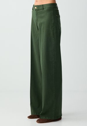 Pantaloni verdi a vita alta dalla gamba larga con bottoni frontali e tasche laterali, indossati con scarpe marroni basse, su uno sfondo semplice.