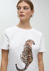 White cotton t-shirt featuring a large sequin-embroidered tiger on the front in shades of brown and gold, with a relaxed fit.