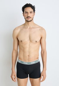Fekete boxernadrág puha elasztikus derékpánttal, zöld Puma logóval. A fazon testhez simuló, sima szövetű.
