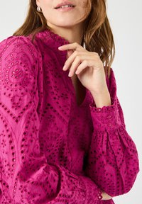 Rosa brodert bluse med hullmønster, med høy hals, puffede ermer og knappdetaljer på mansjettene.
